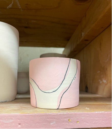 Unglazed ceramic cup mid-decoration, sitting on a workshop shelf.